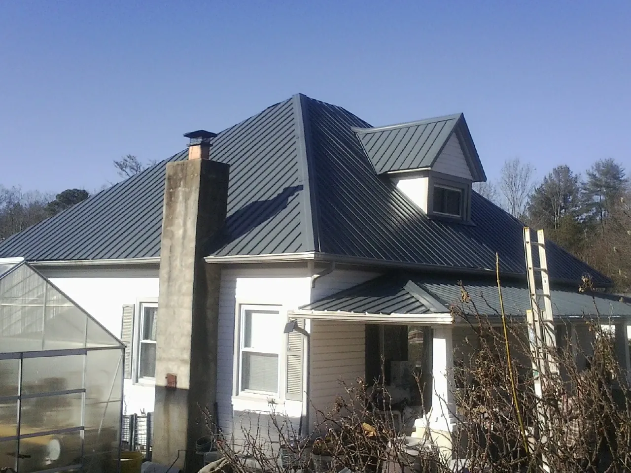 Dark blue standing seam metal roof on a white farmhouse with dormer — Slate & Tile Roof Repair by Roofing Brothers in Grand Terrace