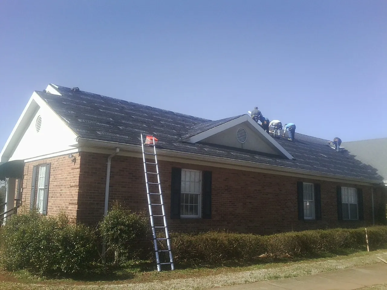 Crew tearing shingles off a brick ranch roof with a ladder set — Metal Roof Repair work by our crew in Grand Terrace