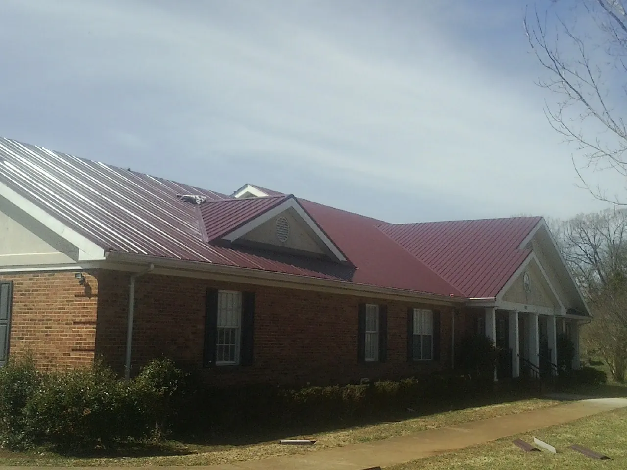 Red metal roof with gabled entries on a long brick building, from a Hail Damage Roof Repair job in Grand Terrace