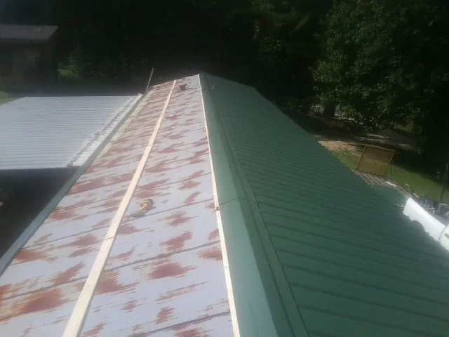 Old rusted panels beside newly installed green metal roofing — Wind Damage Roof Repair by Roofing Brothers in Grand Terrace