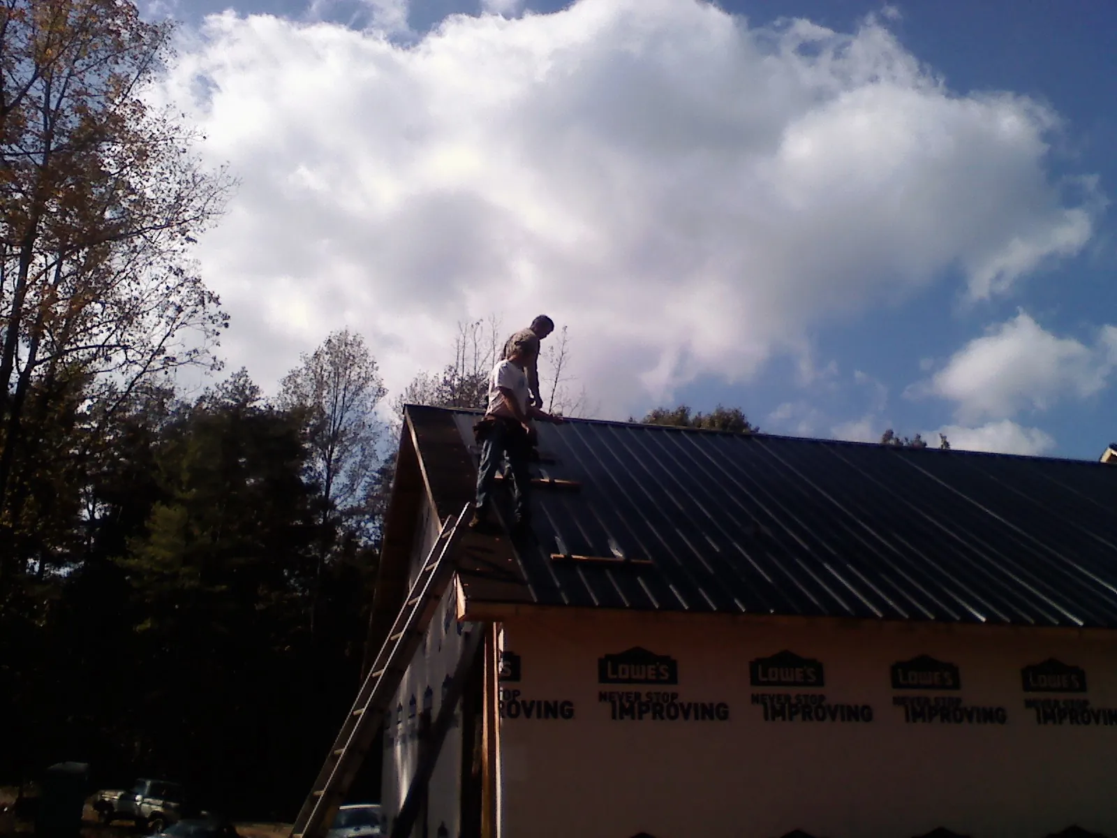 Roofer fastening dark metal panels high against a cloudy sky, from a Roof Inspection job in Grand Terrace