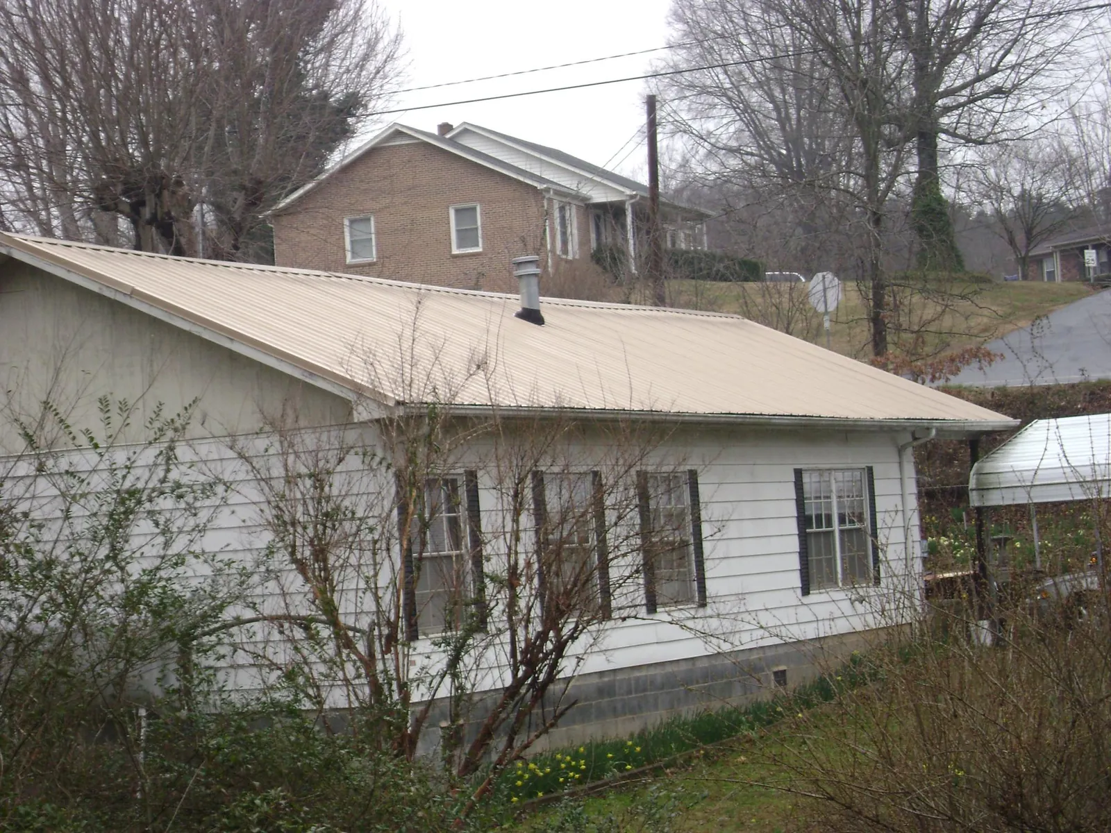 Tan metal roof on a white sided house set into a hillside — Commercial Roofing by Roofing Brothers in Grand Terrace