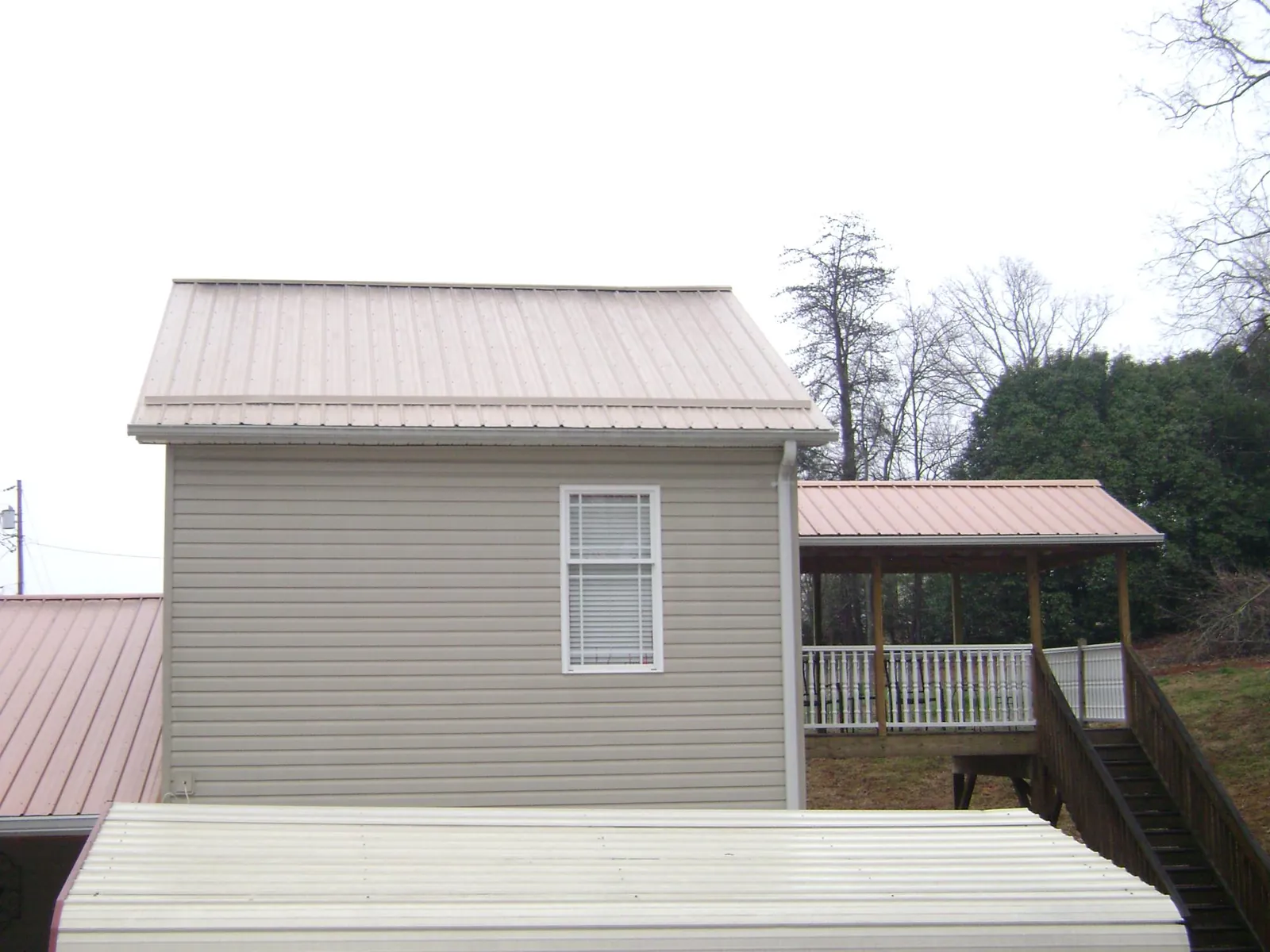 Tan metal roofs on a two story addition and attached porch, from a Roof Replacement job in Grand Terrace
